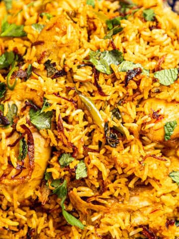 Chicken biryani with herbs and crispy onions in a bowl.