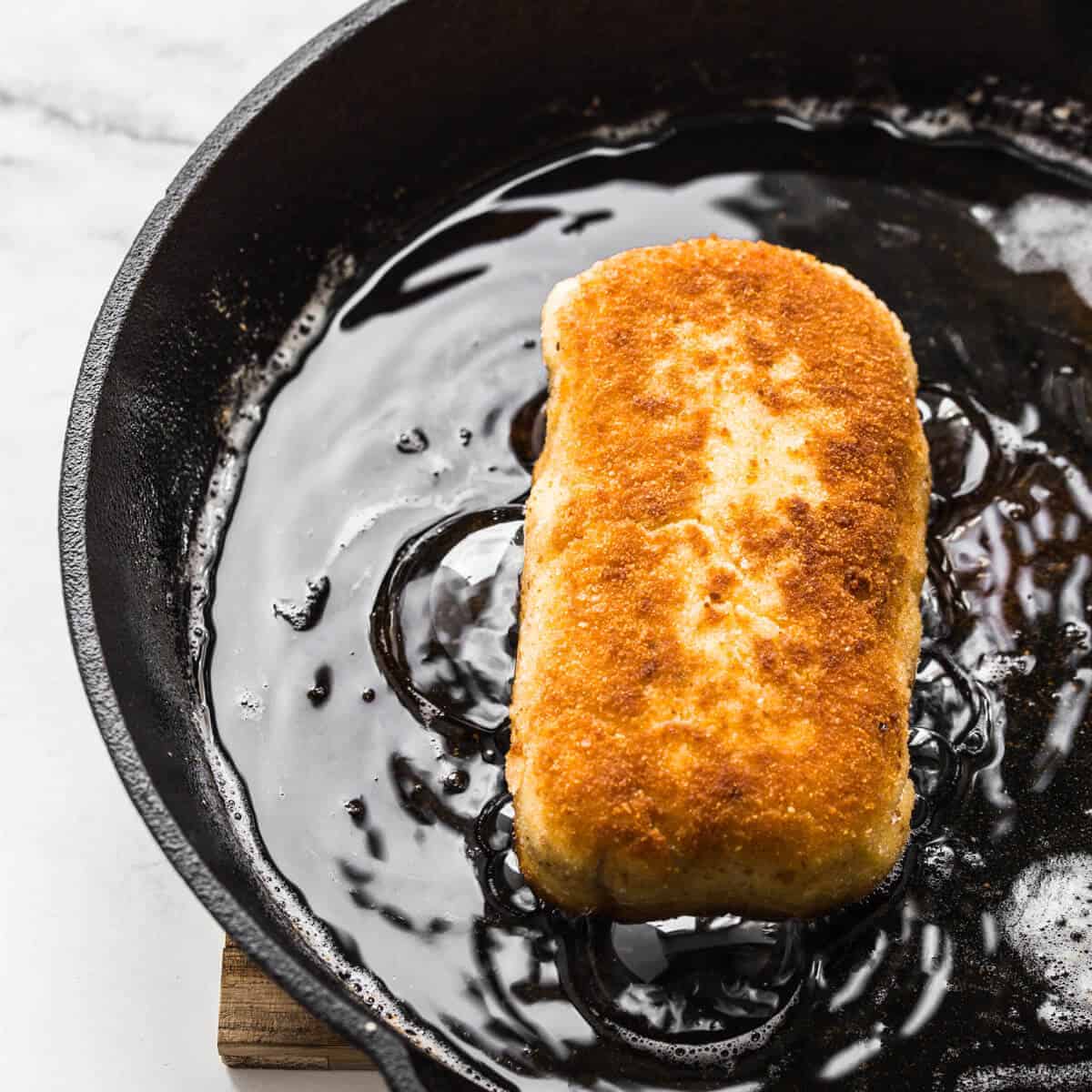 chicken kiev frying in oil in a black skillet