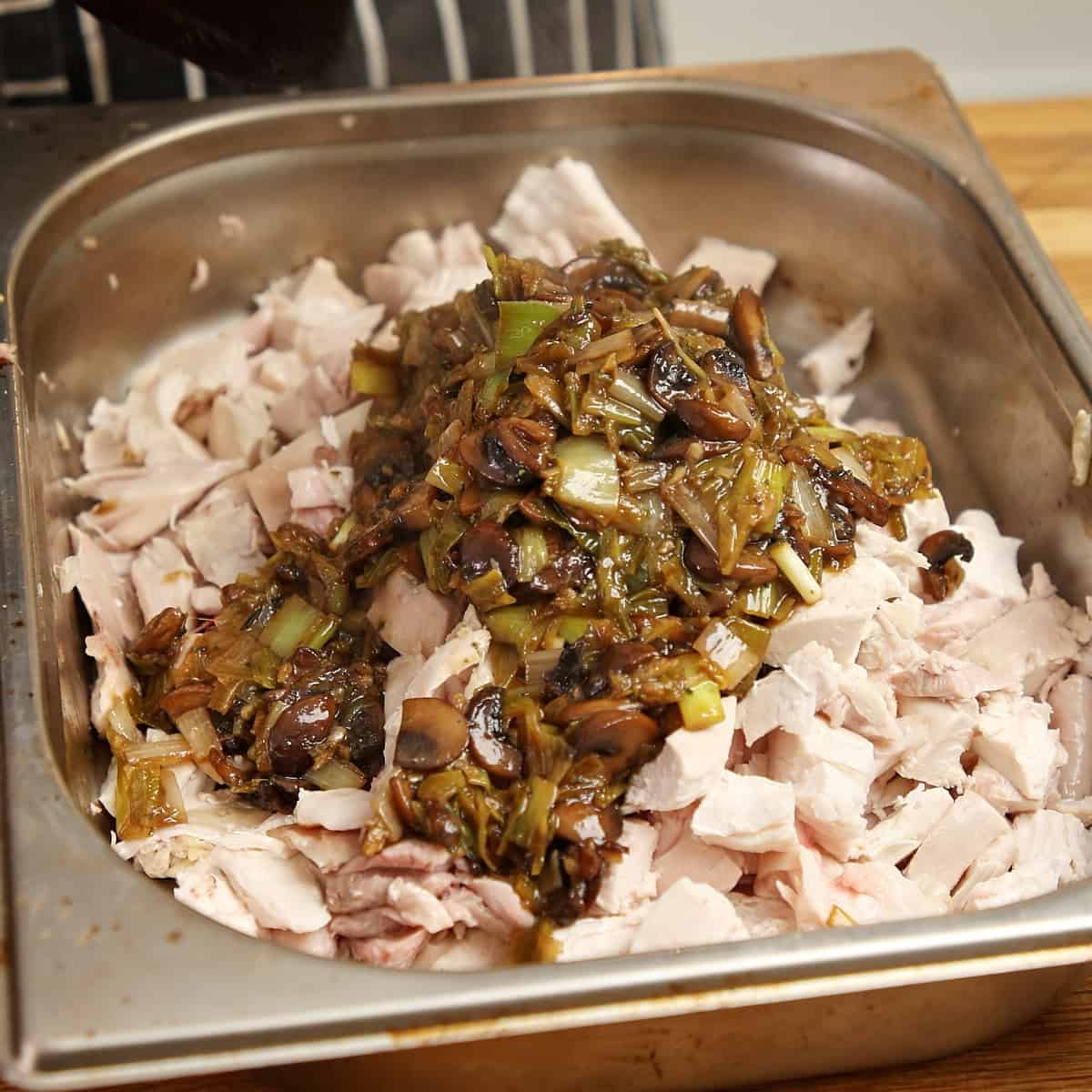 Picked chicken with caramelized leeks and mushrooms in a metal tray.