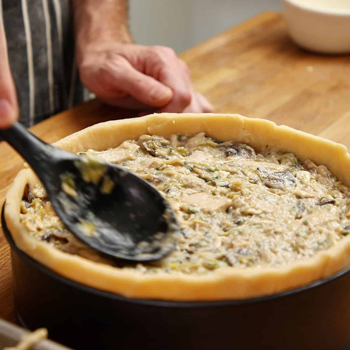 Cold chicken filling being spread into a pastry-lined springform with a spoon.