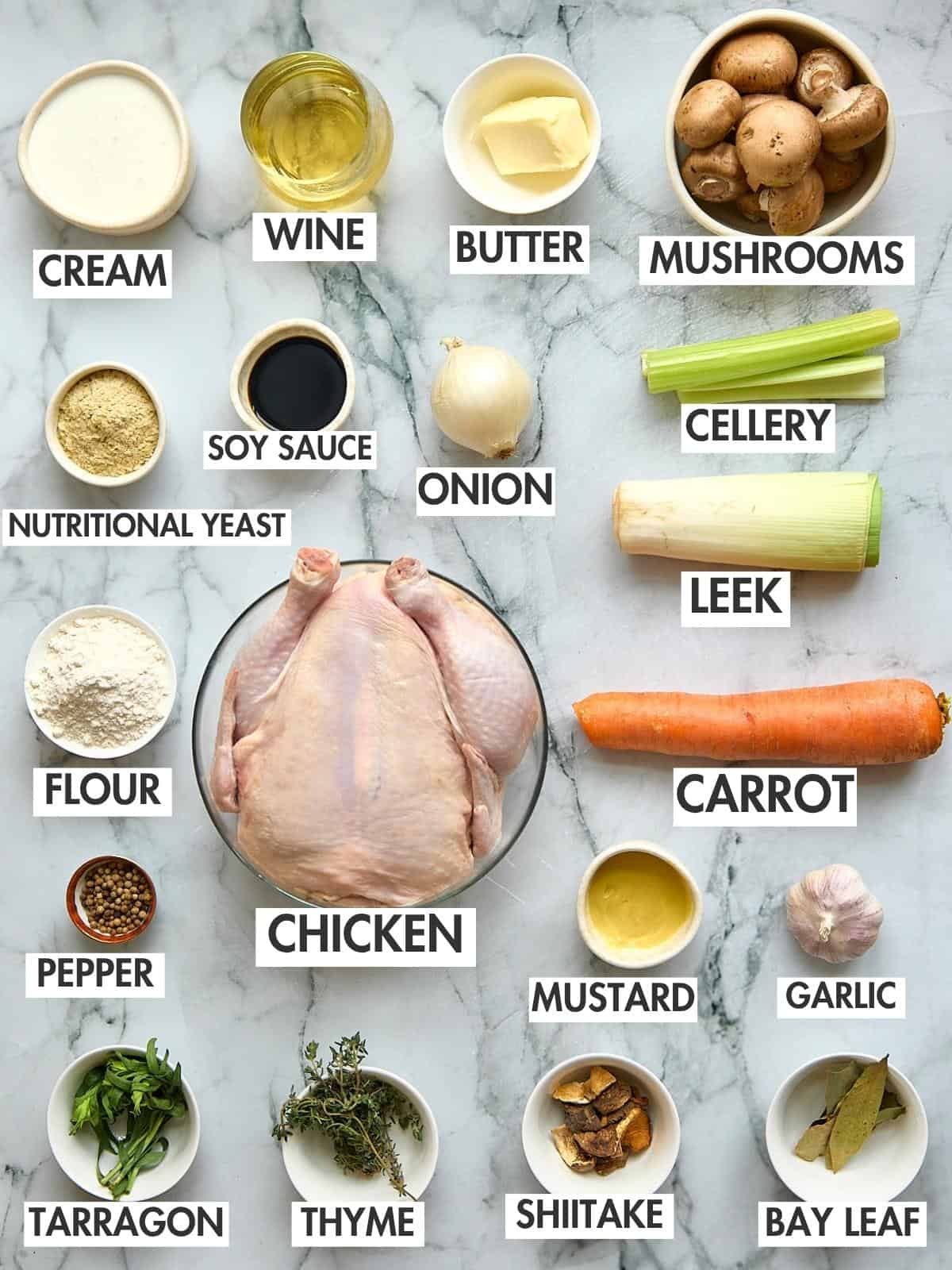 Raw whole chicken surrounded by mise en place ingredients including mushrooms, celery, carrot, onion, and herbs on marble surface.