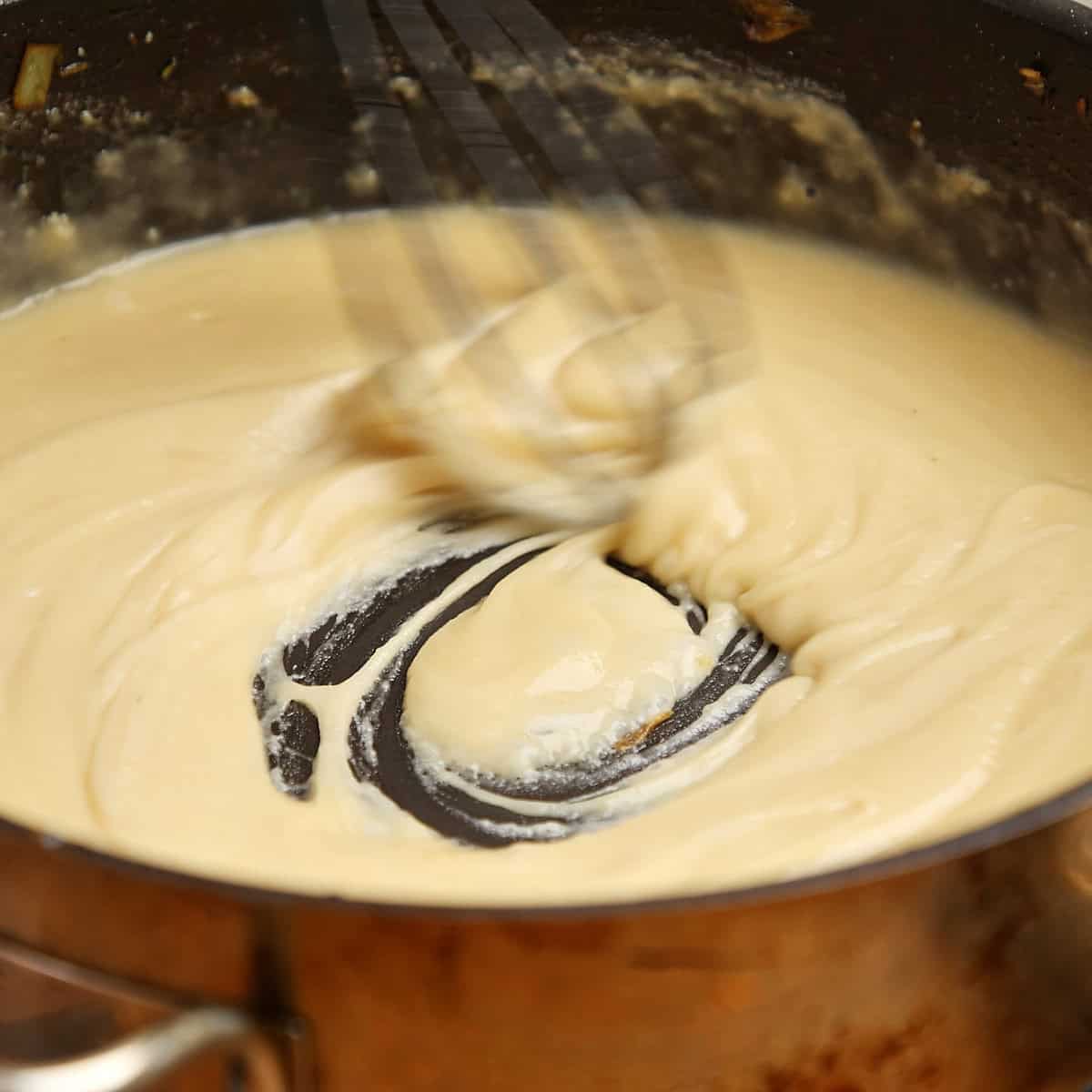 Smooth velouté sauce being whisked in a copper pot.