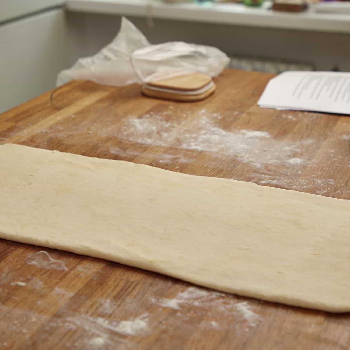 Chilled pastry slab on floured surface being pressed with rolling pin to flatten before rolling.