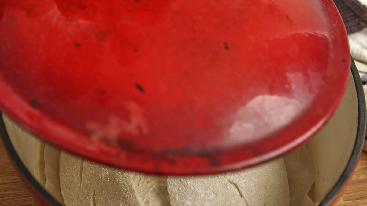 A red lid closing a dutch oven with sourdough bread inside.