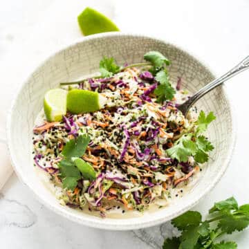 Coleslaw with tahini dressing in white bowl on marble background.