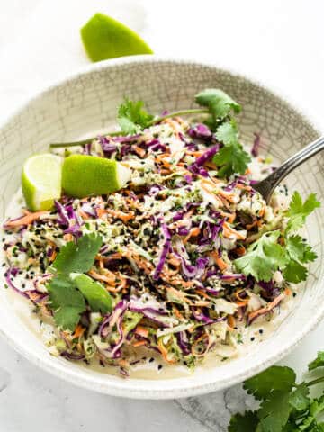 Coleslaw with tahini dressing in white bowl on marble background.