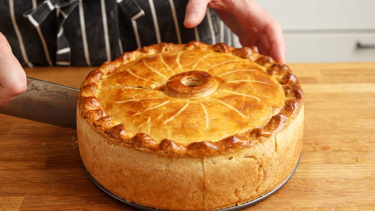 Knife cutting a slice from a deep golden baked chicken pie.