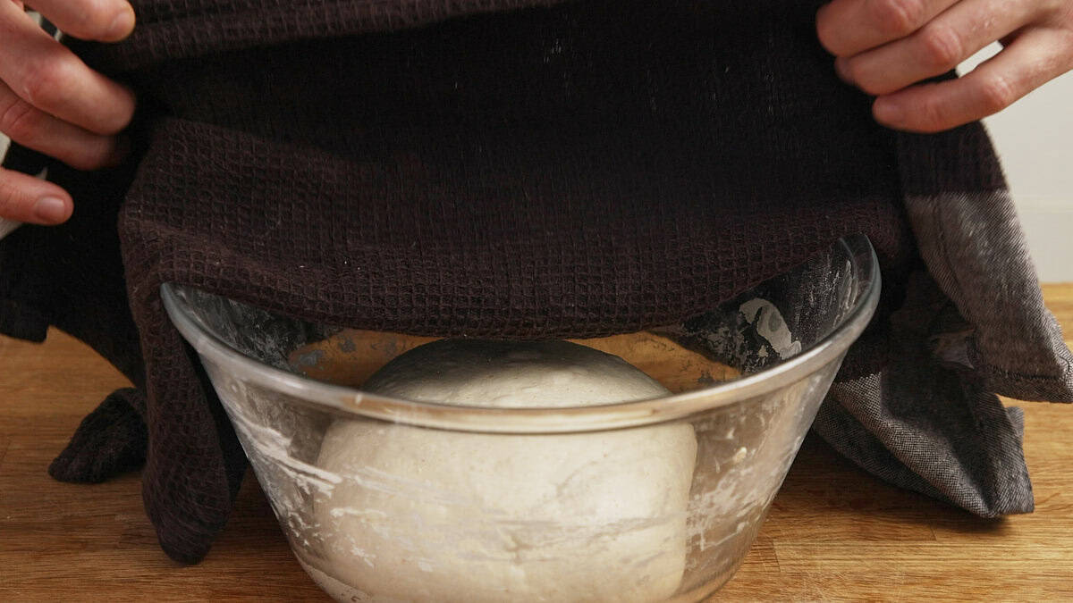 Damp cloth covering dough in a glass bowl.