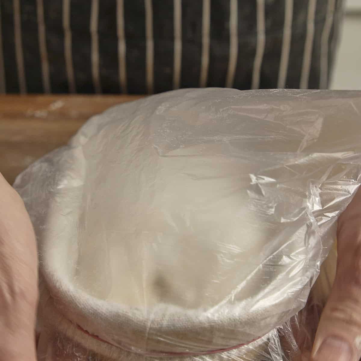 Closing a proving basket containing sourdough with a plastic bag.
