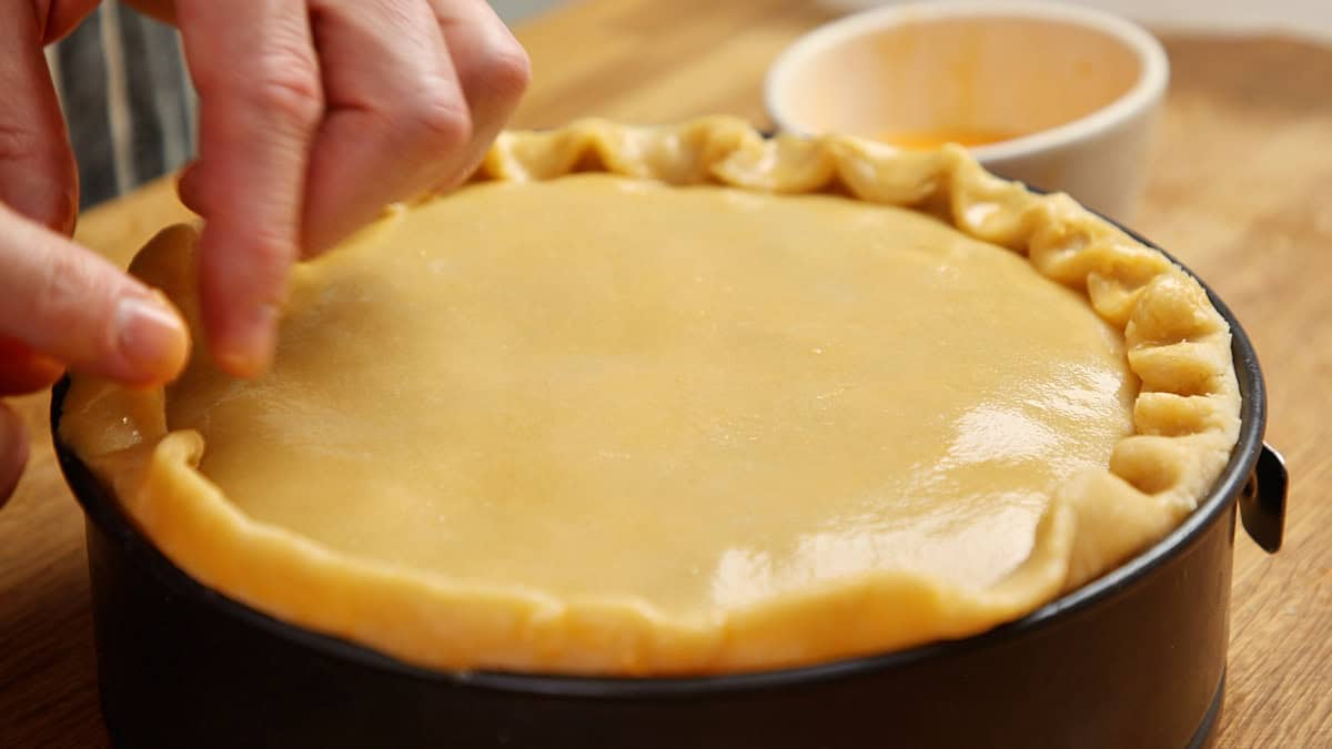 A hand crimping the fluted edge of an unbaked chicken pie in a springform.