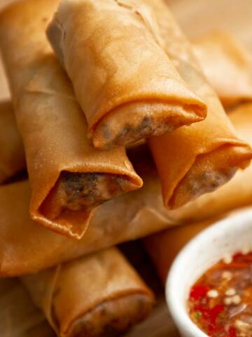 Stack of crispy spring rolls with dipping sauce on a wooden board.