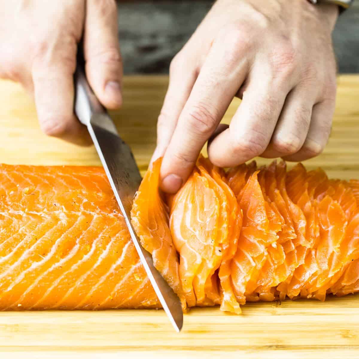 slicing cured salmon gravlax on a wooden board