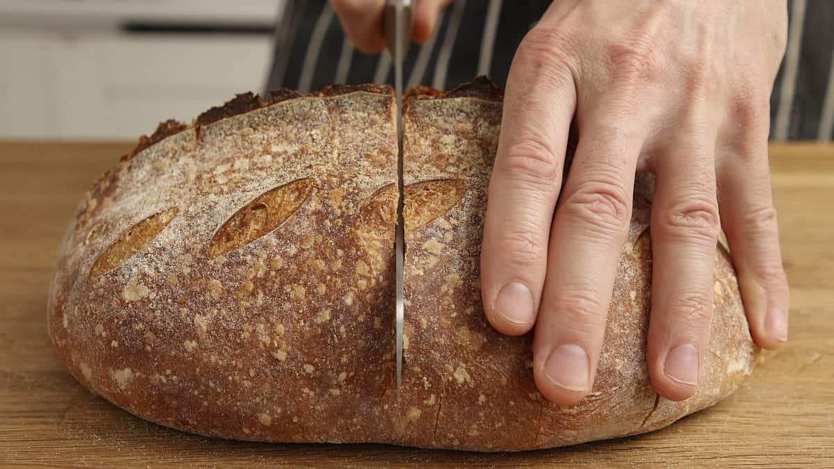 Slicing a loaf of bread with a bread knife on a wooden table.