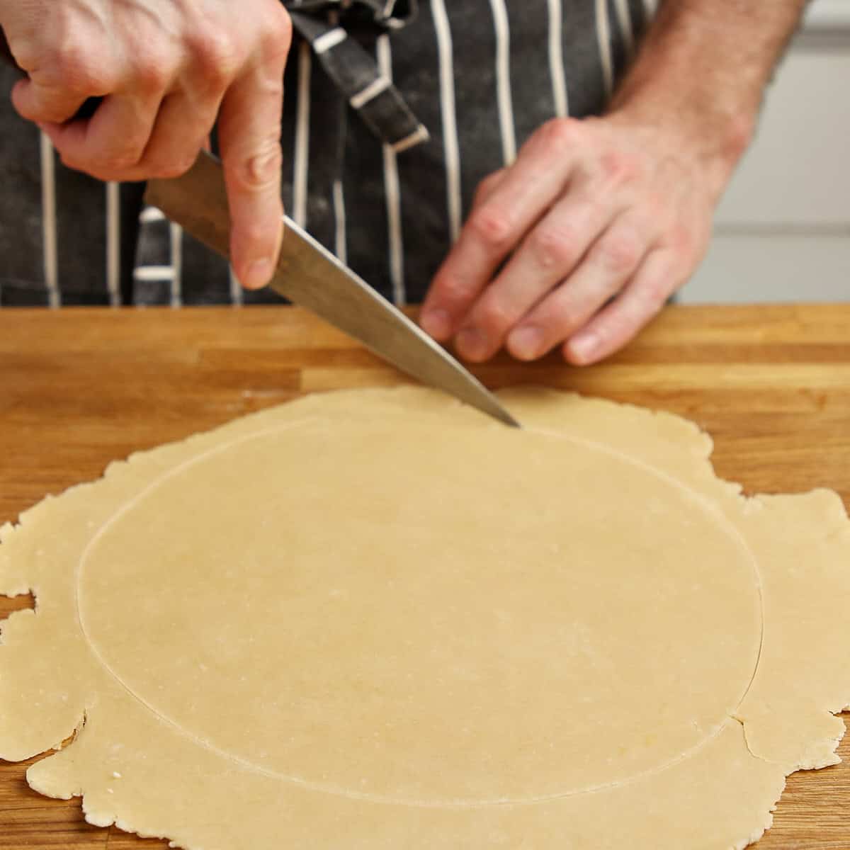 Cutting a clean circle from rolled pastry with a knife.