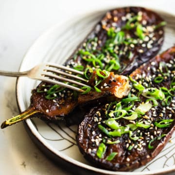 miso baked eggplant with spring onion and toasted sesame seeds and green onion on white plate