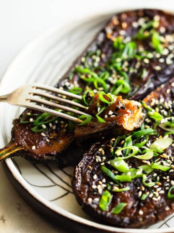 miso baked eggplant with spring onion and toasted sesame seeds and green onion on white plate