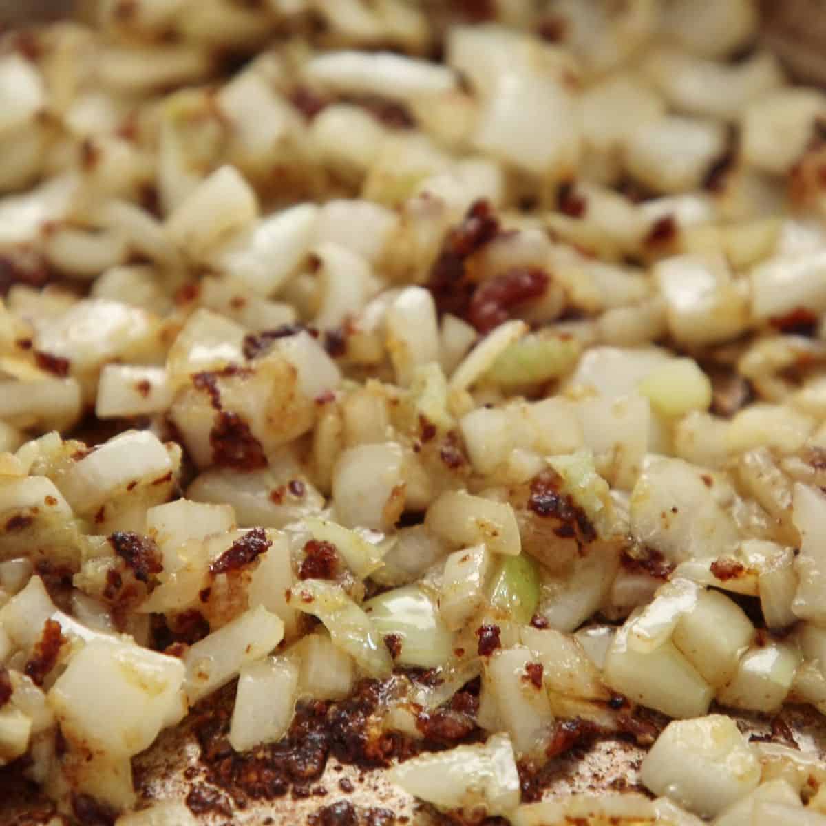 Diced onions and minced garlic cooking in pot with visible brown fond on bottom being scraped up