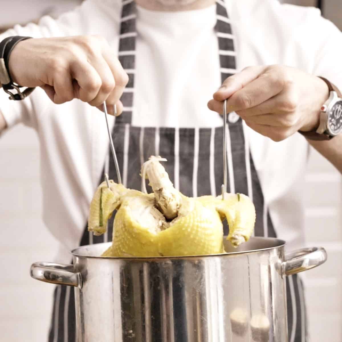 Dipping chicken into broth using two meat hooks.