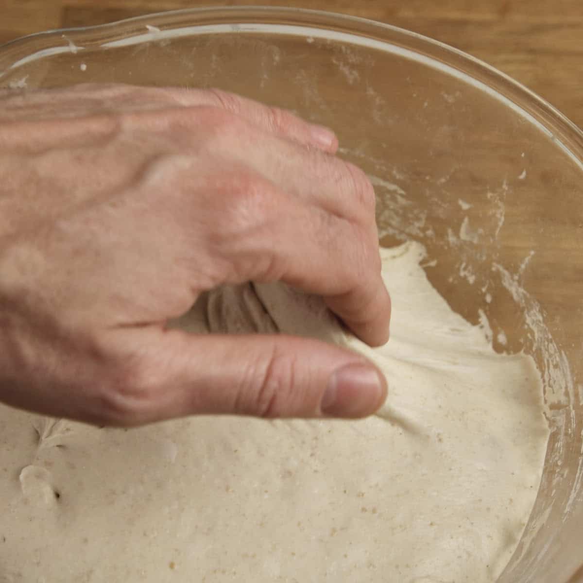 Pulling proven sourdough away from the sides of a glass bowl.