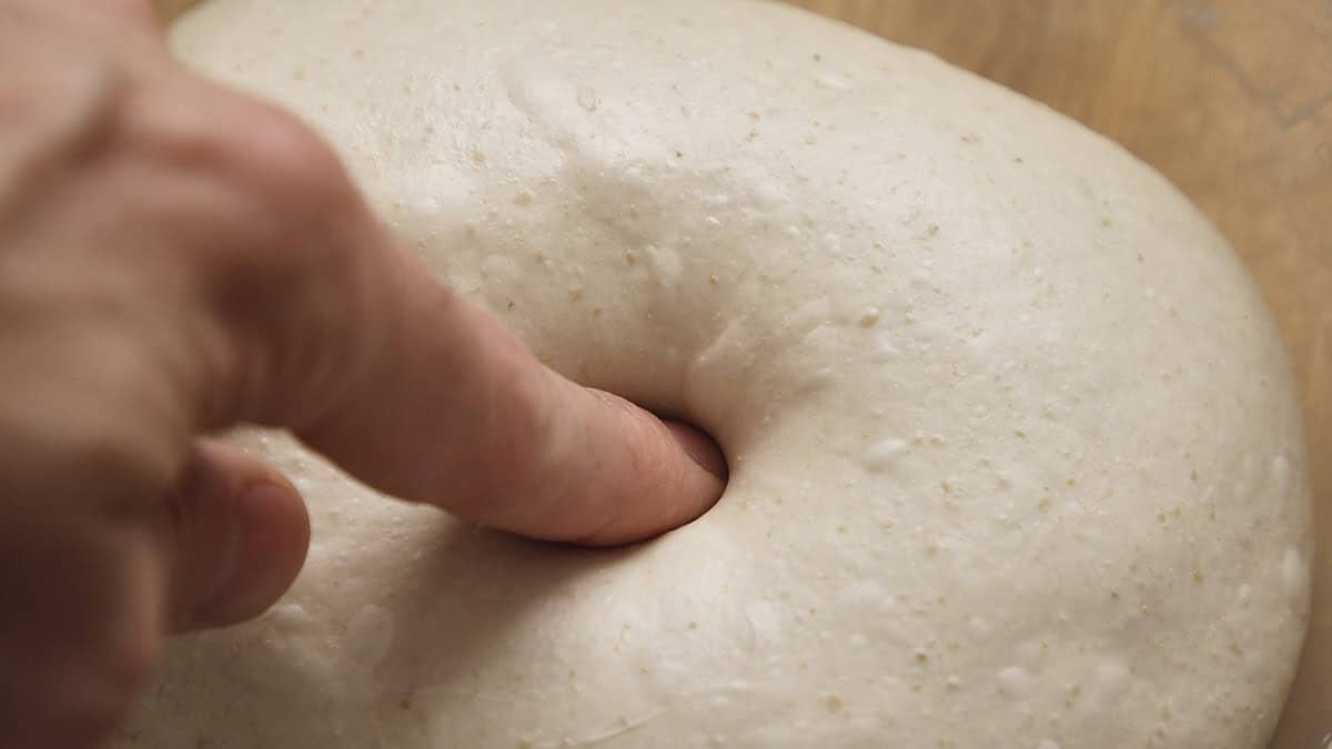 Finger poking into a smooth dough ball.