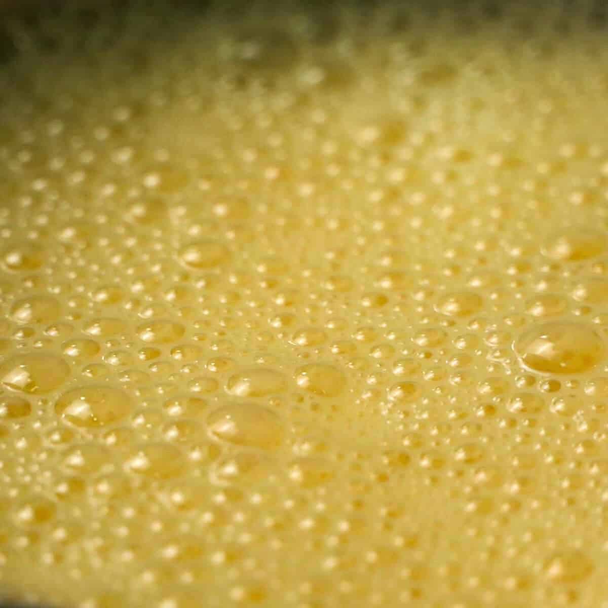 Frothy beaten egg close up in metal bowl.