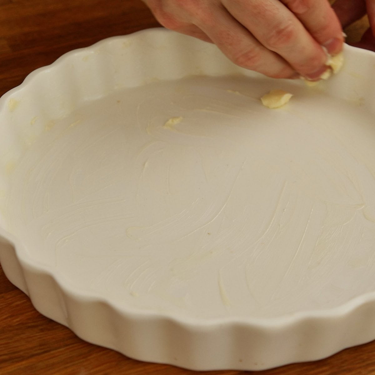 Hands buttering a fluted ceramic tart tin.