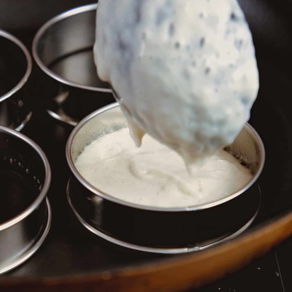 Crumpet batter in black pan and steel rings.