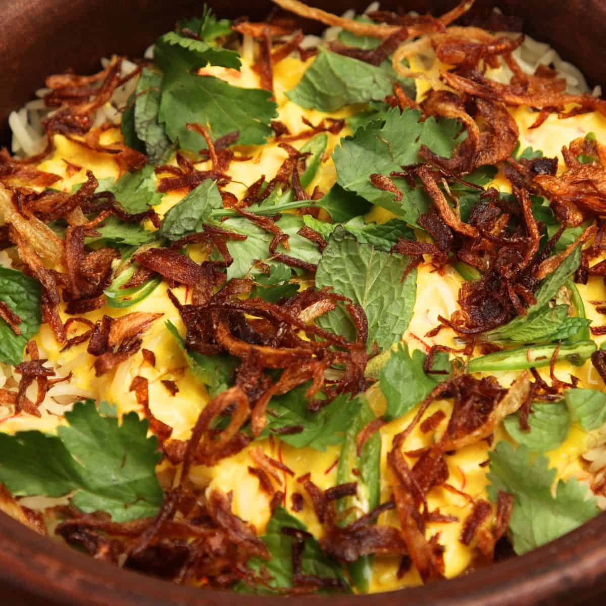 Final layer of biryani with crispy onions, herbs, and saffron sauce on rice.