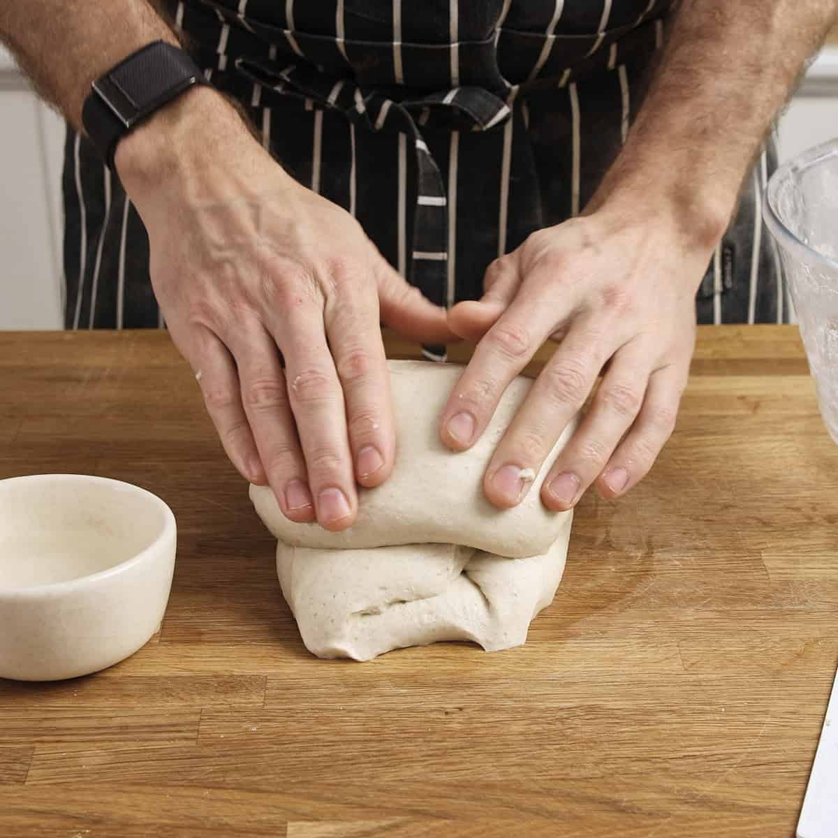 Rolling dough forward on wooden bench to build tension.