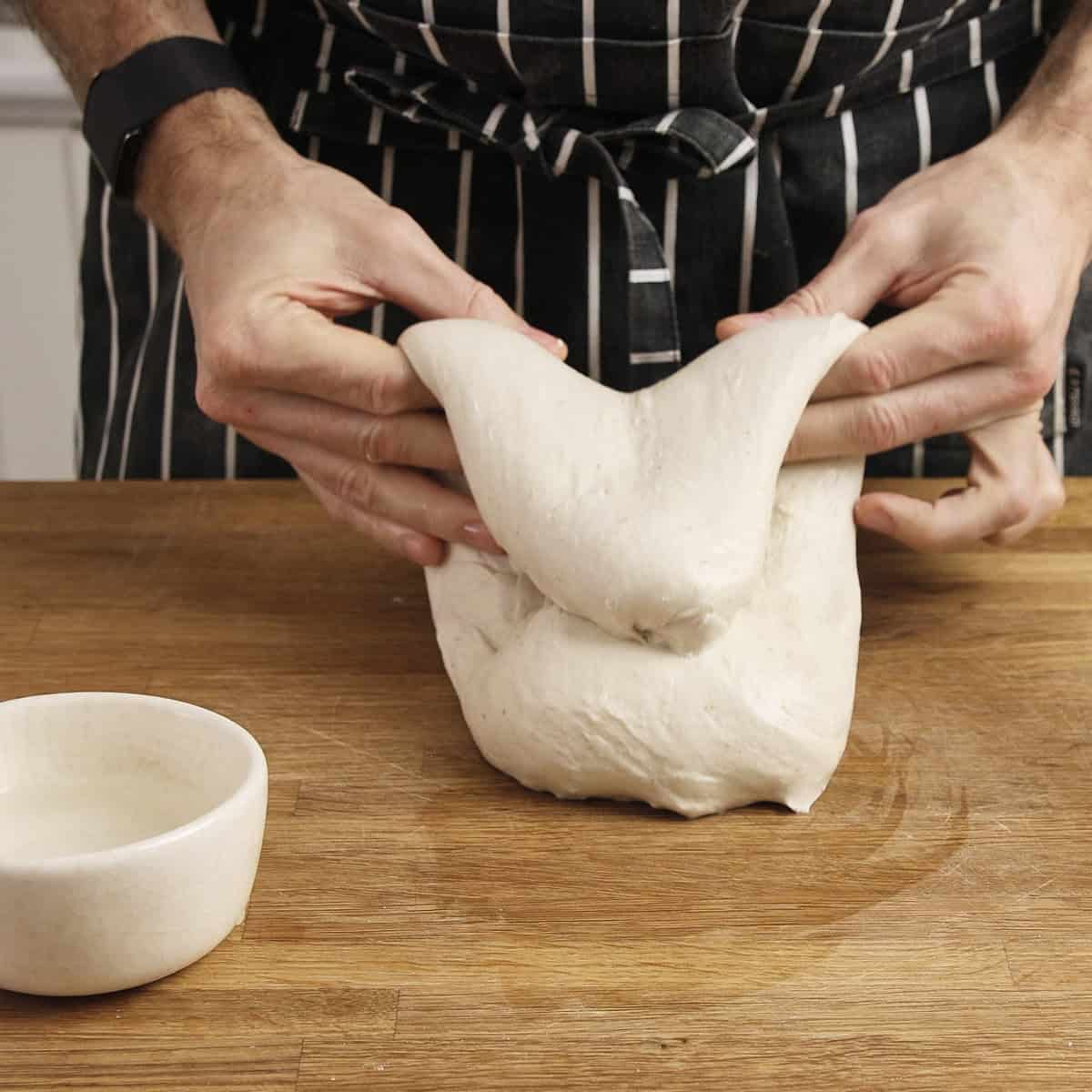 Performing a slap and fold on dough by first pinching the sides in the middle of the dough.