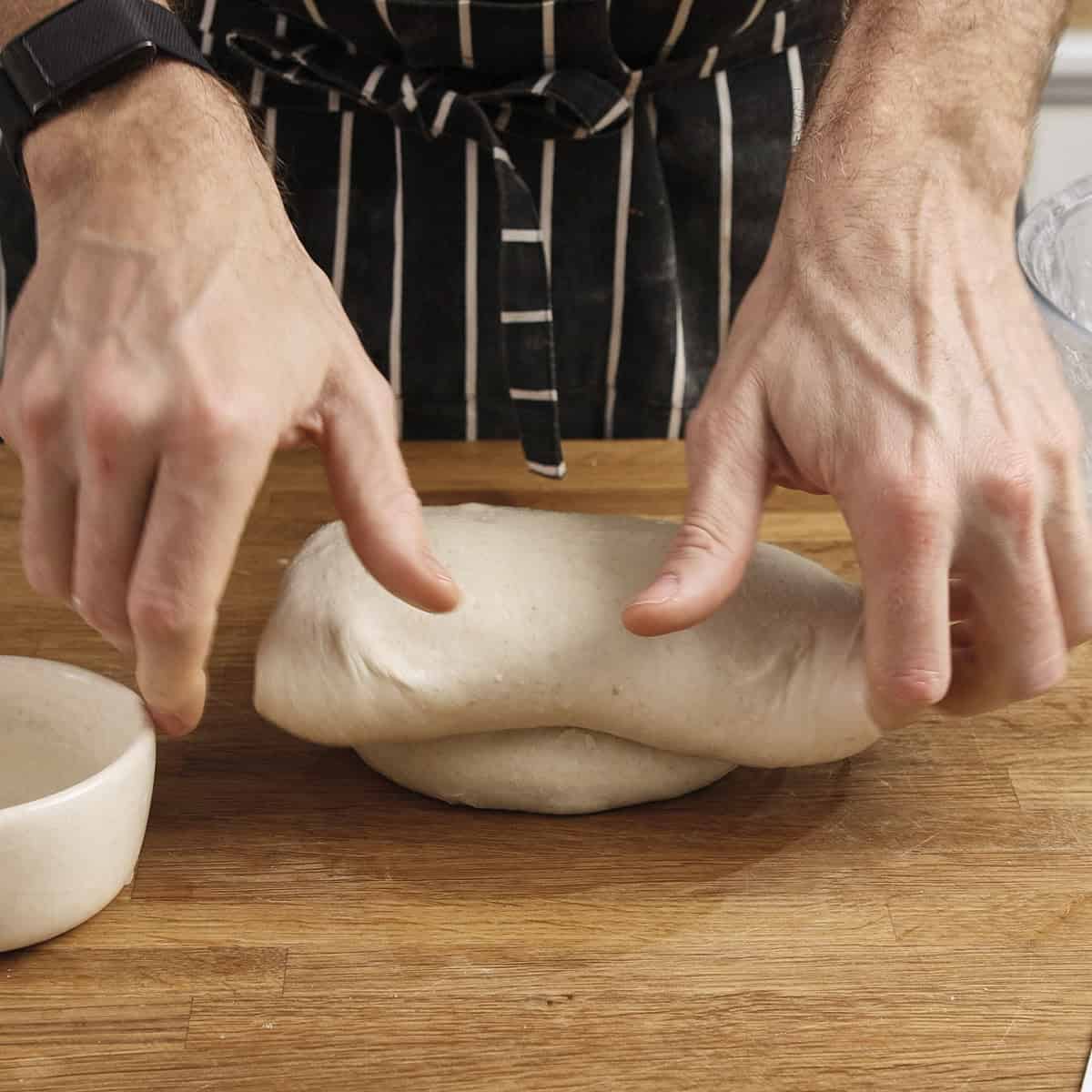 Hands shape sourdough on a wooden surface.
