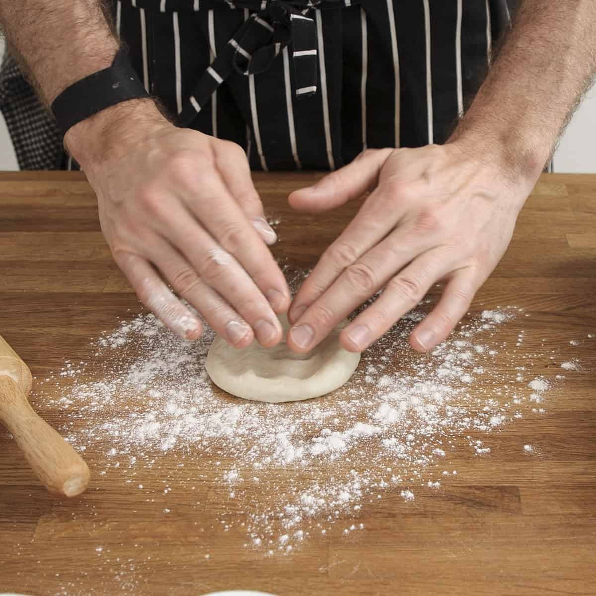Flattening naan dough by hand on a floured surface.