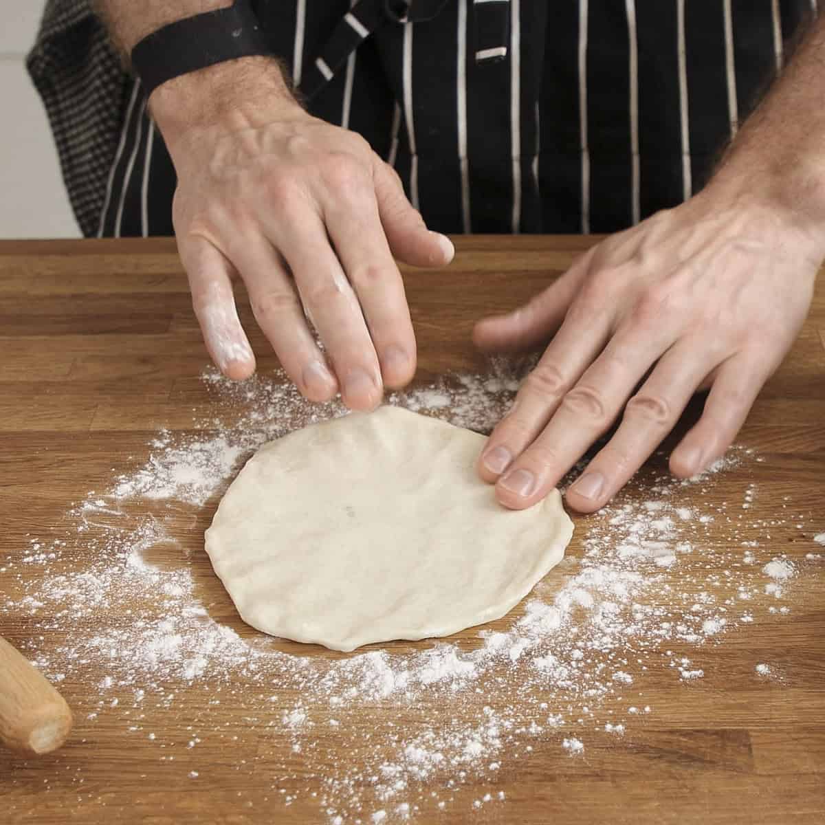 Flattening naan dough by hand on a floured surface.
