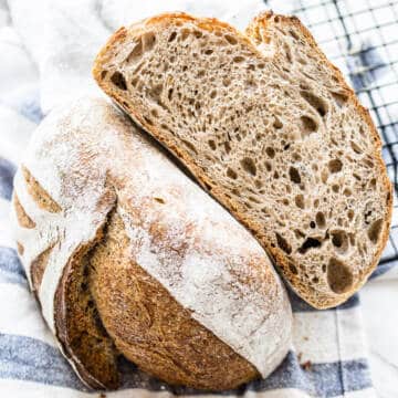 flaxseed meal sourdough bread cut in half on striped kitchen towel