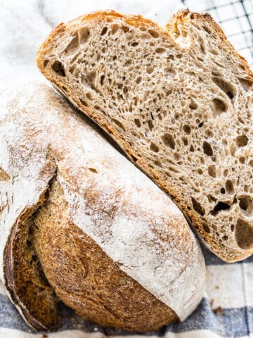 flaxseed meal sourdough bread cut in half on striped kitchen towel