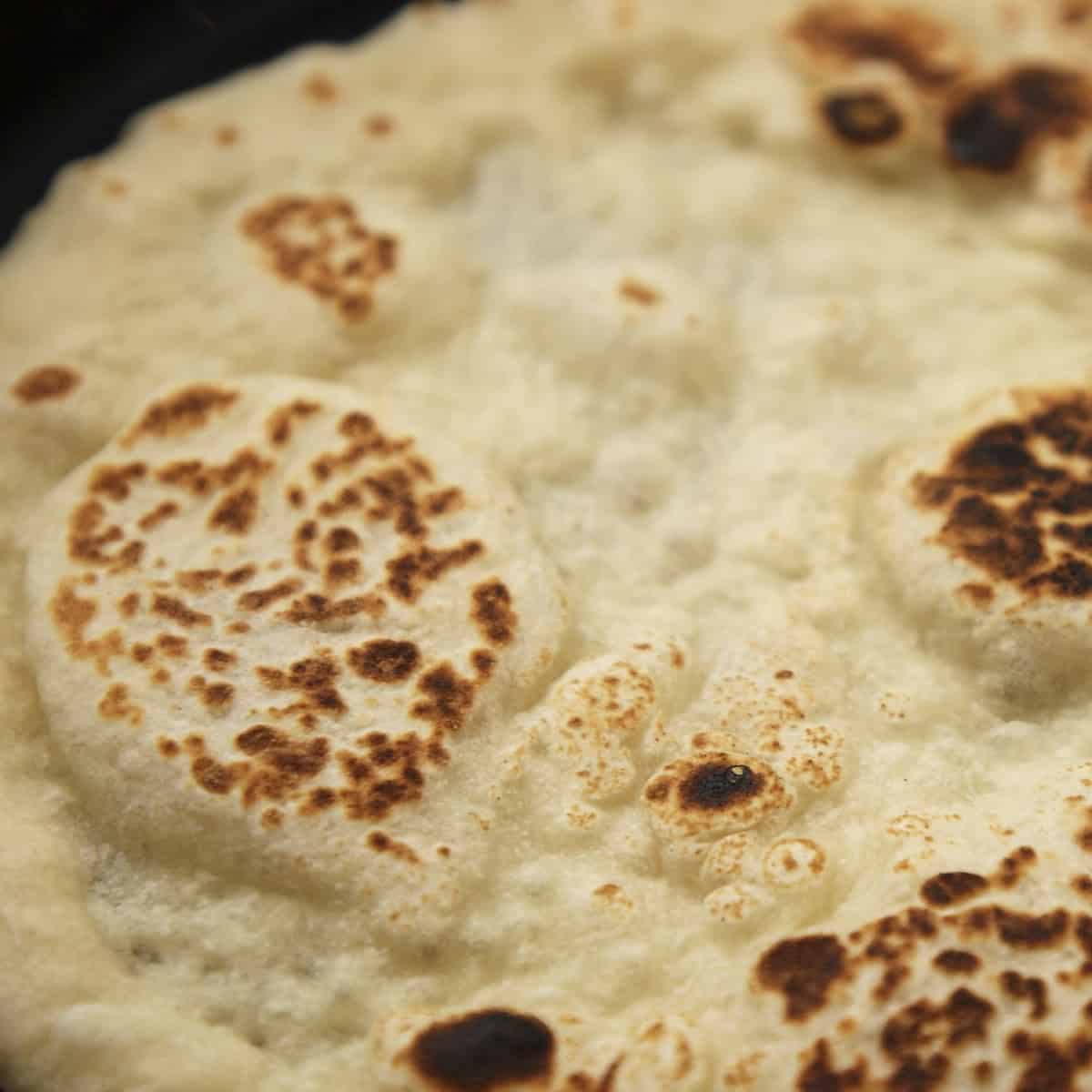 Blistered and charred naan in a black skillet