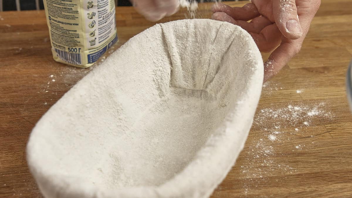 Sprinkling rice flour into a linen lined proving basket.