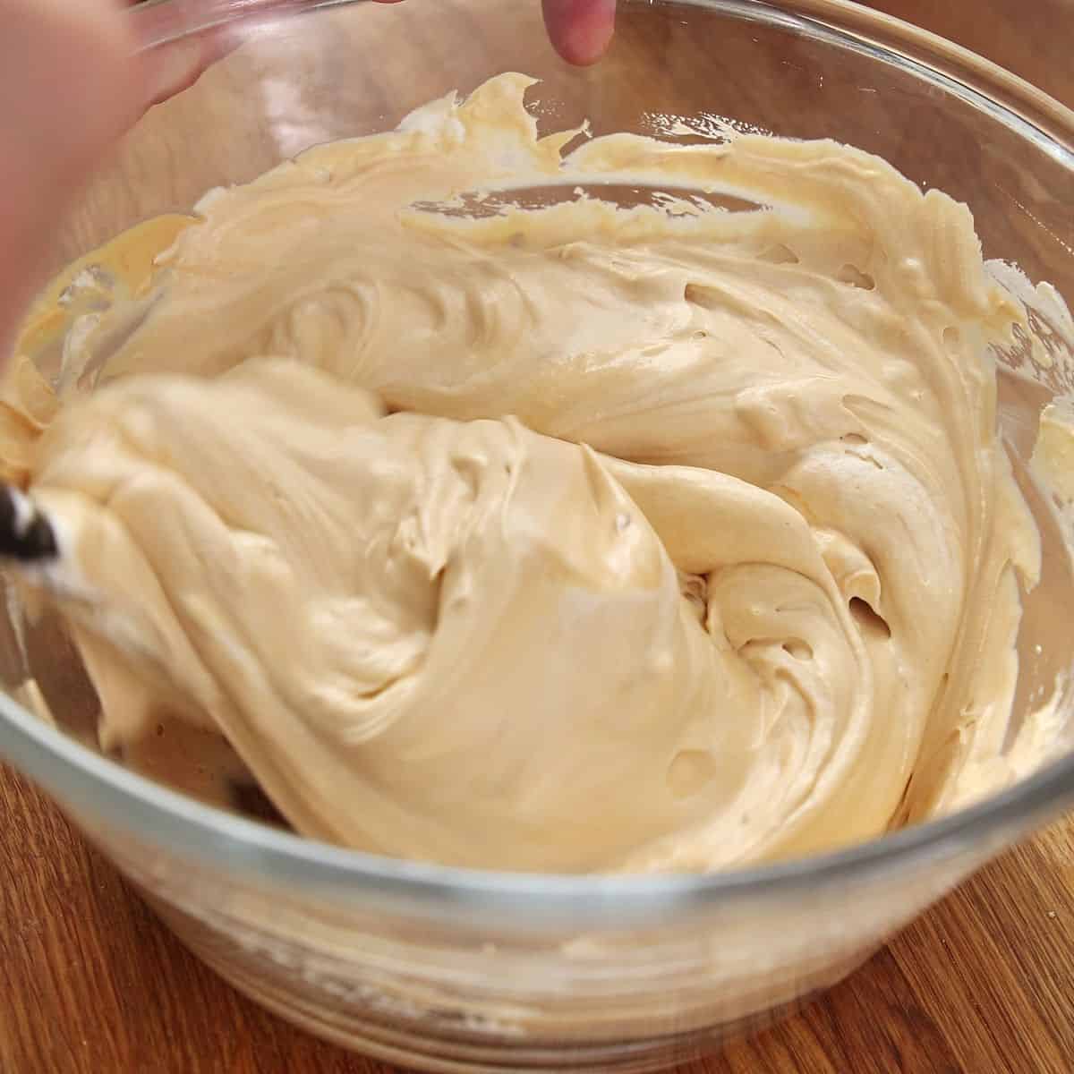 Folding remaining whipped cream into lightened caramel mixture with large spatula, showing marbled appearance mid-fold with gradual incorporation.