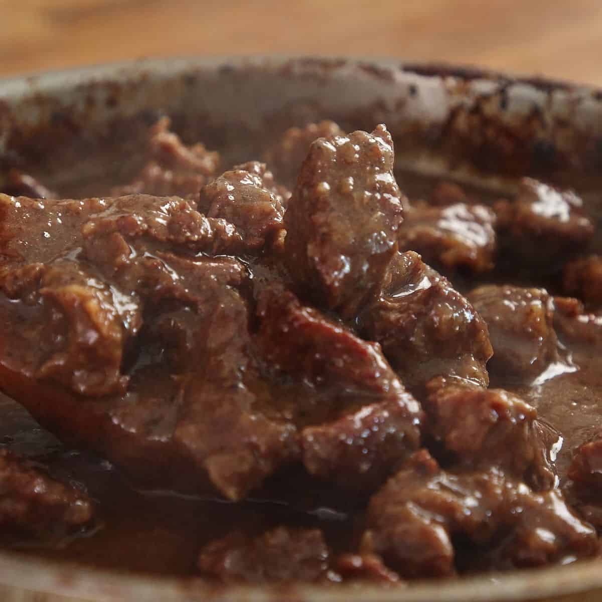 Fork-tender braised beef being shredded slightly in pot, showing glossy gravy and some larger chunks remaining