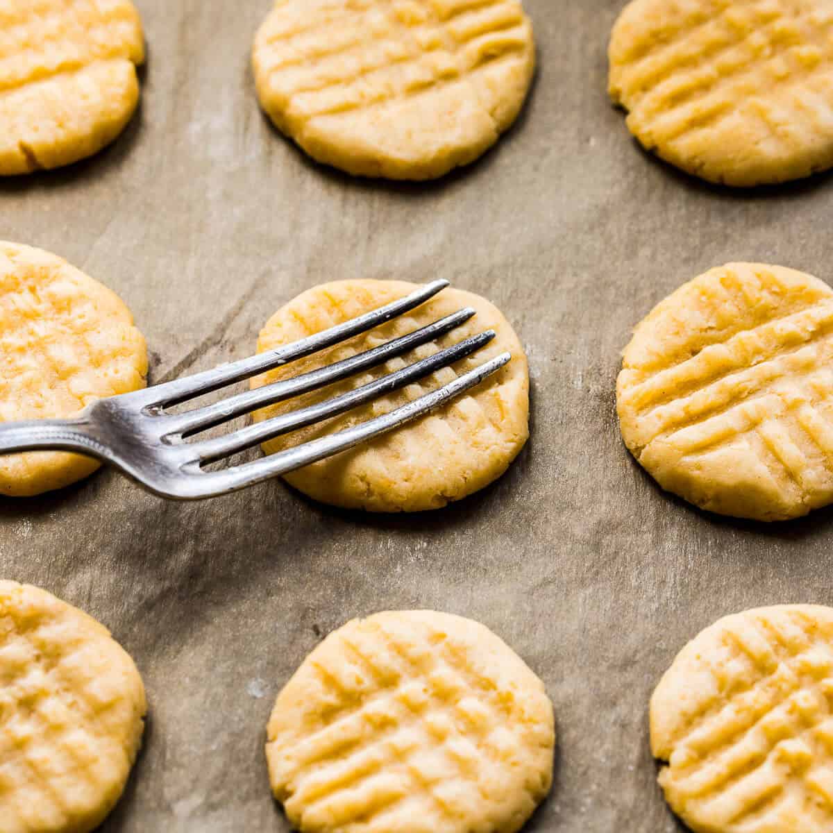 Fork pressing down Parmesan cookies to create a criss cross patern.