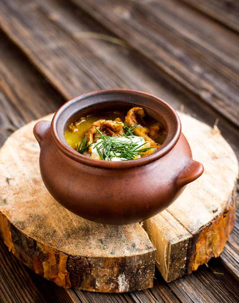 Chanterelle mushroom soup in a brown bowl on wooden table.