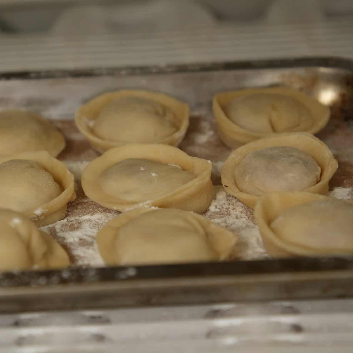 Frozen pelmeni on a parchment lined tray.