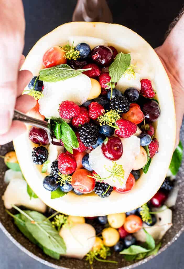 fresh fruit salad bowl with melon, berries, cherries , mint and dill blossom.