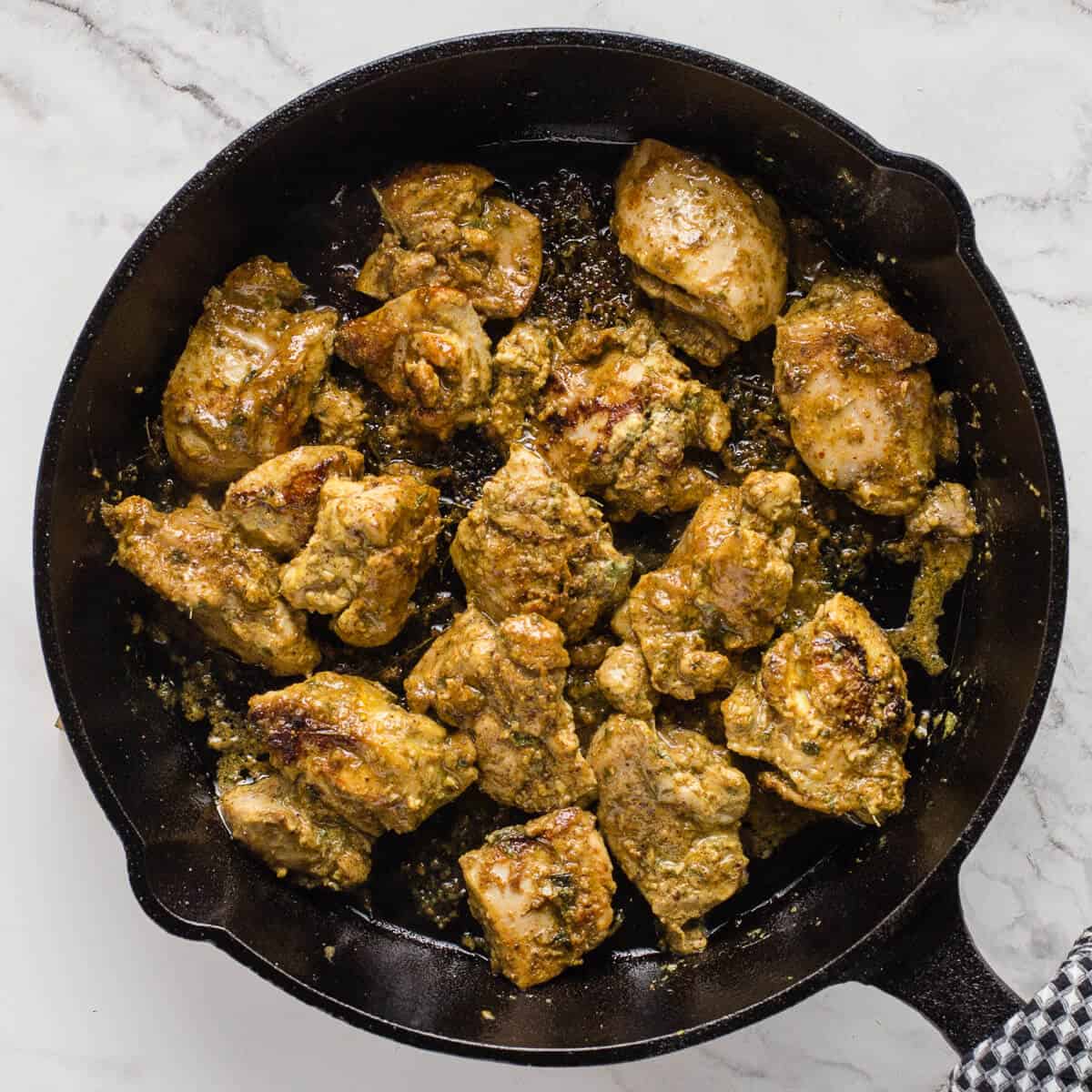 Marinated chicken pieces frying in a cast iron pan.