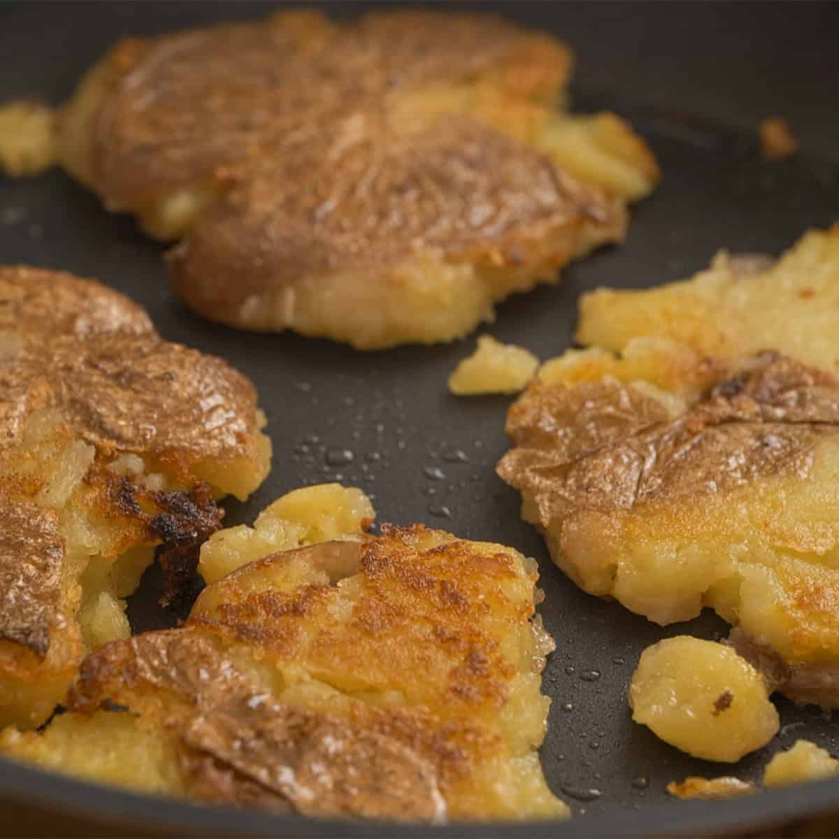 Frying smashed potatoes in a pan with olive oil.