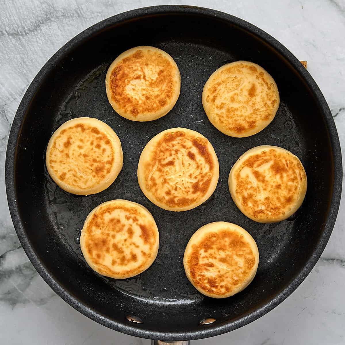 Fried syrniki in a black pan.