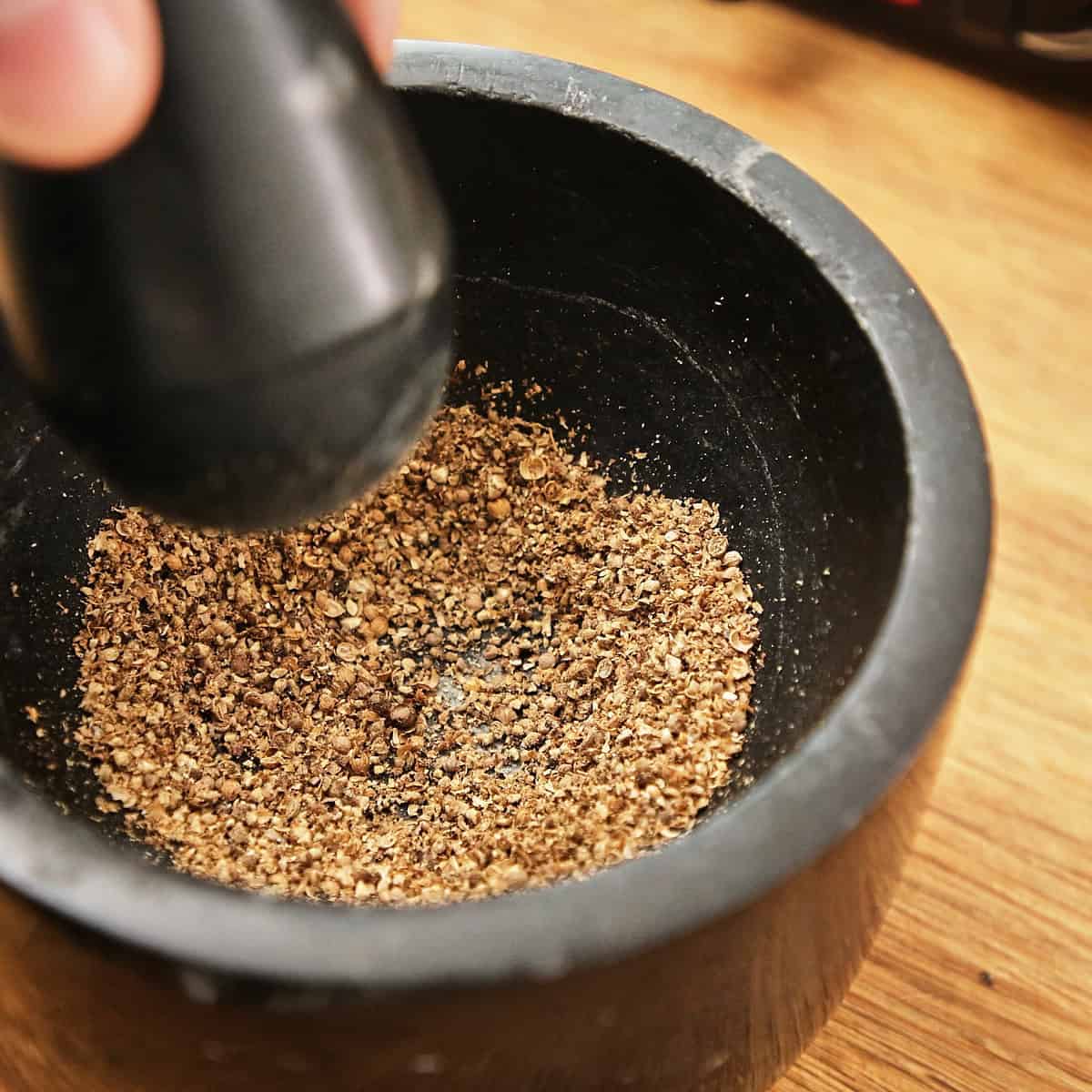 Ground coriander and other spices being crushed with a pestle in a mortar.
