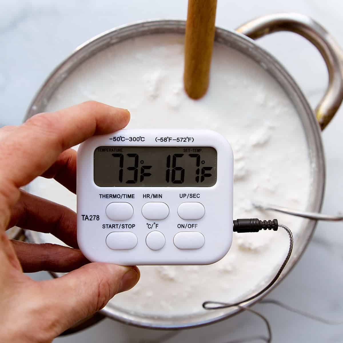 Kitchen thermometer showing the temperature of cheese curds in a pot.