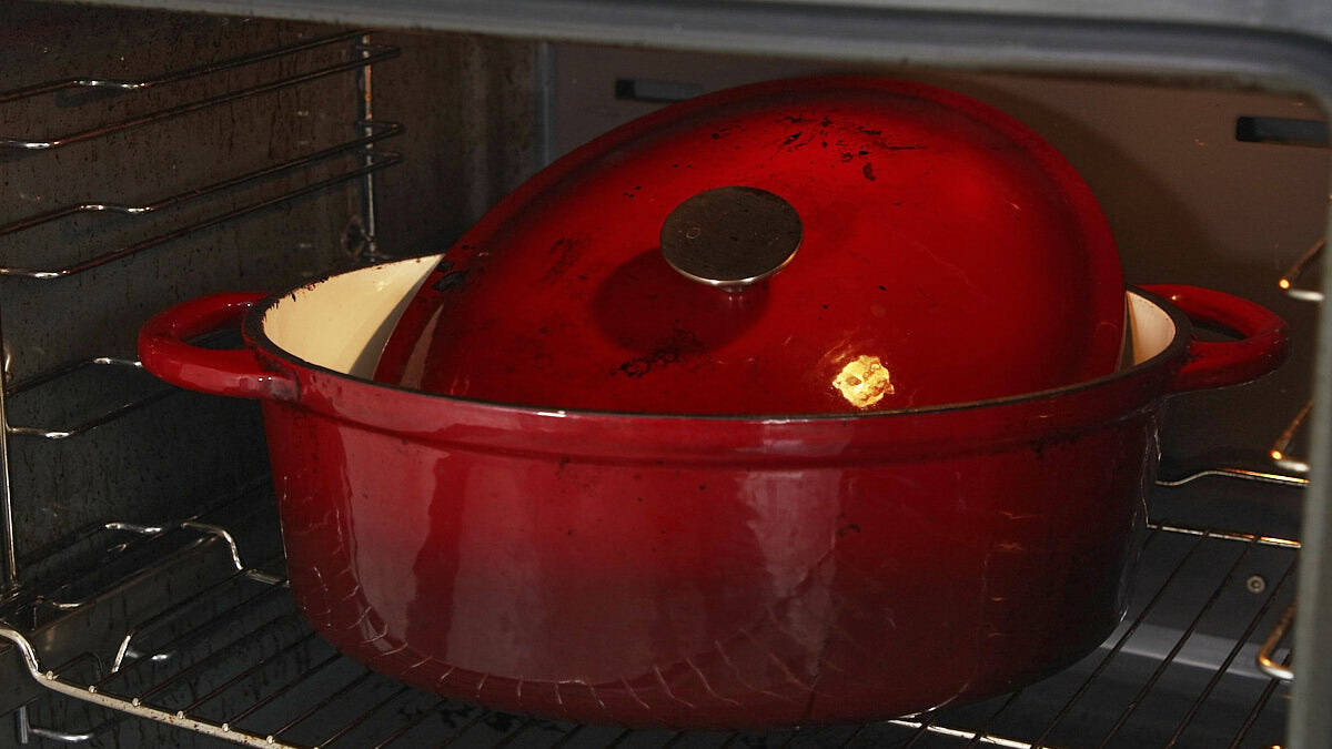 A red baking pot sits inside an oven.