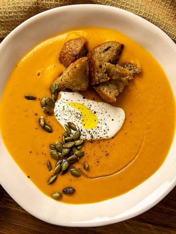Pumpkin cream soup with crispy croutons, cream and pumpkin seeds in a white bowl.